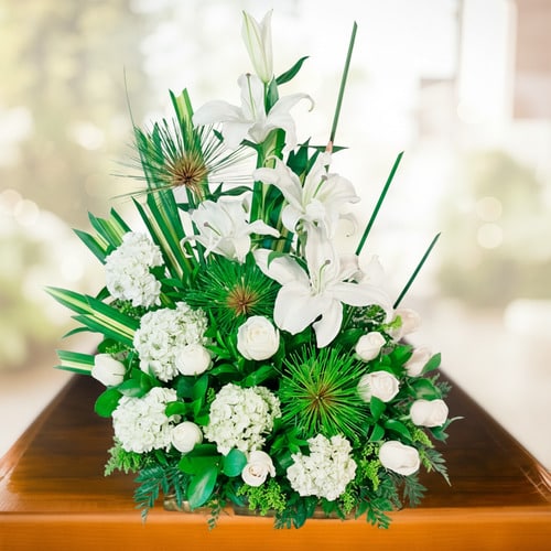 Arreglo de flores blancas con lirios, rosas y hortensias sobre una mesa de madera, con fondo desenfocado