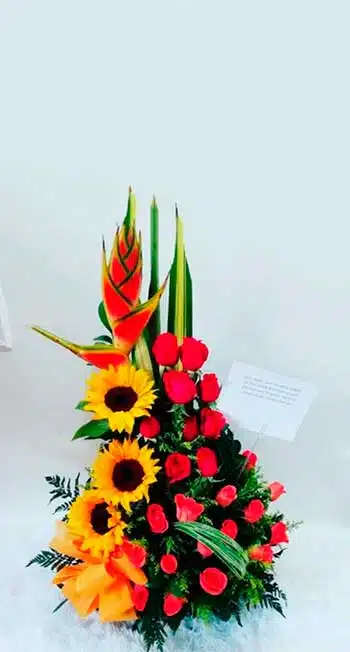 Arreglo floral fúnebre con rosas y lirios blancos frente a un ataúd de madera en una sala velatoria