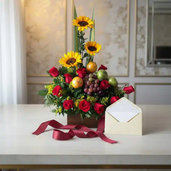Arreglo floral Batista con rosas rojas, girasoles vibrantes, uvas y manzanas verdes, sobre mesa de mármol con tarjeta de rega