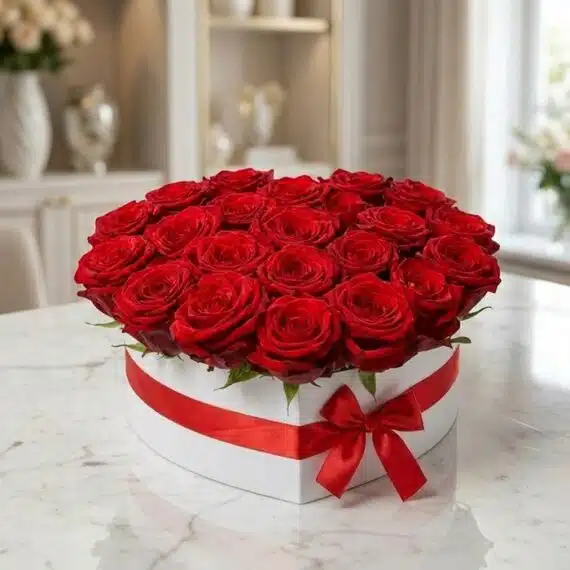 Arreglo Floral CAMILA: 24 Rosas Premium Rojas en Caja Corazón Blanca Arreglo floral CAMILA con 24 rosas rojas premium en una elegante caja blanca en forma de corazón, adornada con un lazo rojo,