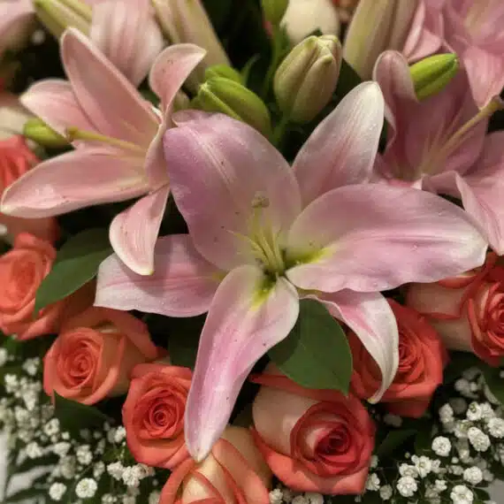 Primer plano extremo de un arreglo floral 'Feliz Contigo' con lirios rosados, rosas coral y pequeñas flores blancas, mostrand