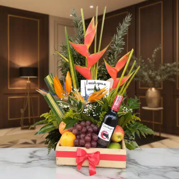 Arreglo Floral con Frutas Platonia y Vino Tinto para Regalar Arreglo floral Platonia con heliconias, aves del paraíso, uvas, manzanas, duraznos y botella de vino tinto, sobre mármol en u