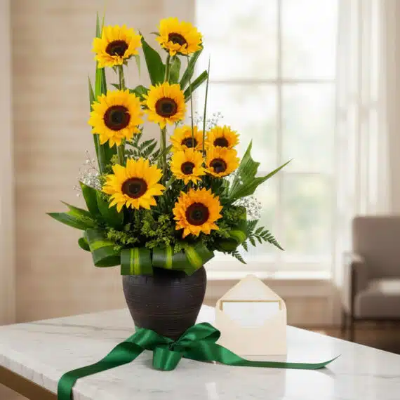 Arreglo floral GIULIANA con girasoles radiantes en jarrón oscuro, sobre mármol, con tarjeta de regalo y cinta verde satinada,