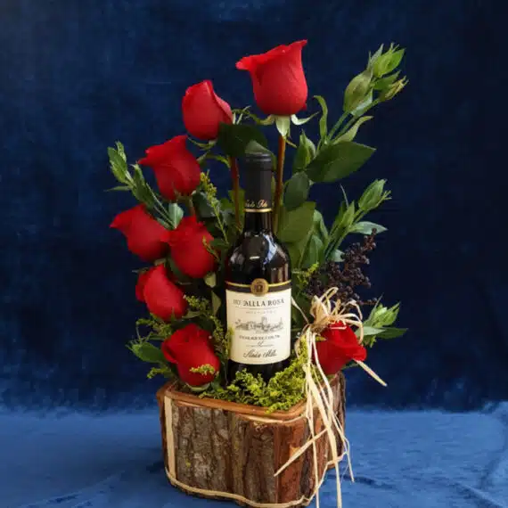 Arreglo Floral VERITA: Rosas Rojas y Vino para un Regalo Apasionado Arreglo floral VERITA con rosas rojas frescas y una botella de vino tinto, presentado en una base de madera rústica, ideal pa