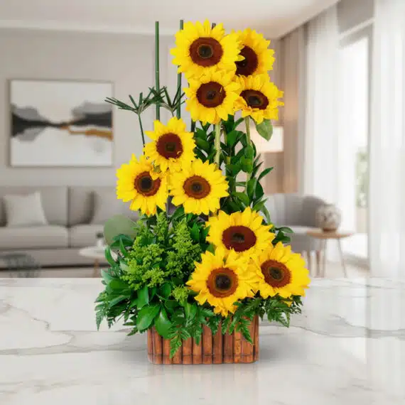 Arreglo con Girasoles Verano sobre Mármol: Frescura y Elegancia Floral Arreglo floral con girasoles vibrantes y follaje verde en una base de madera, sobre una superficie de mármol pulido en un ent