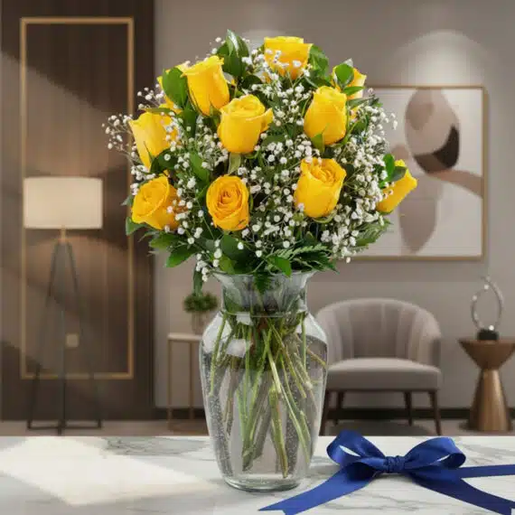 Jarrón de cristal con doce rosas amarillas frescas y gypsophila, sobre una mesa de mármol con un lazo azul marino, en un ambi
