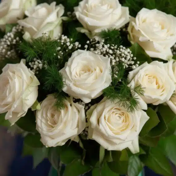 Primer plano extremo de un jarrón con rosas blancas frescas, con gotas de rocío sutiles y follaje verde, destacando la textur